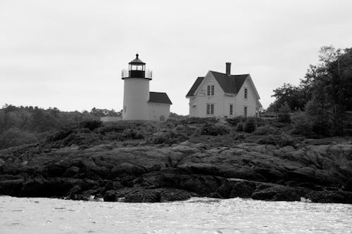 Grayscale Photo of Lighthouse Near a House