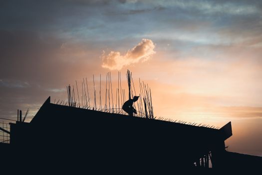 A silhouette of a construction worker working on a rooftop during a vivid sunset.