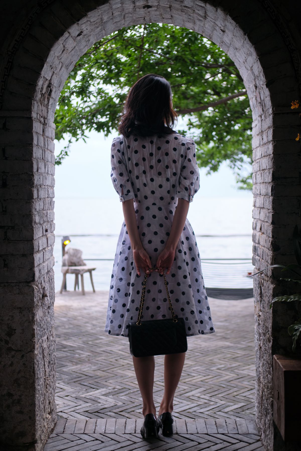 A woman in a black and white polka dot dress standing under a concrete arch — graphic elegance
