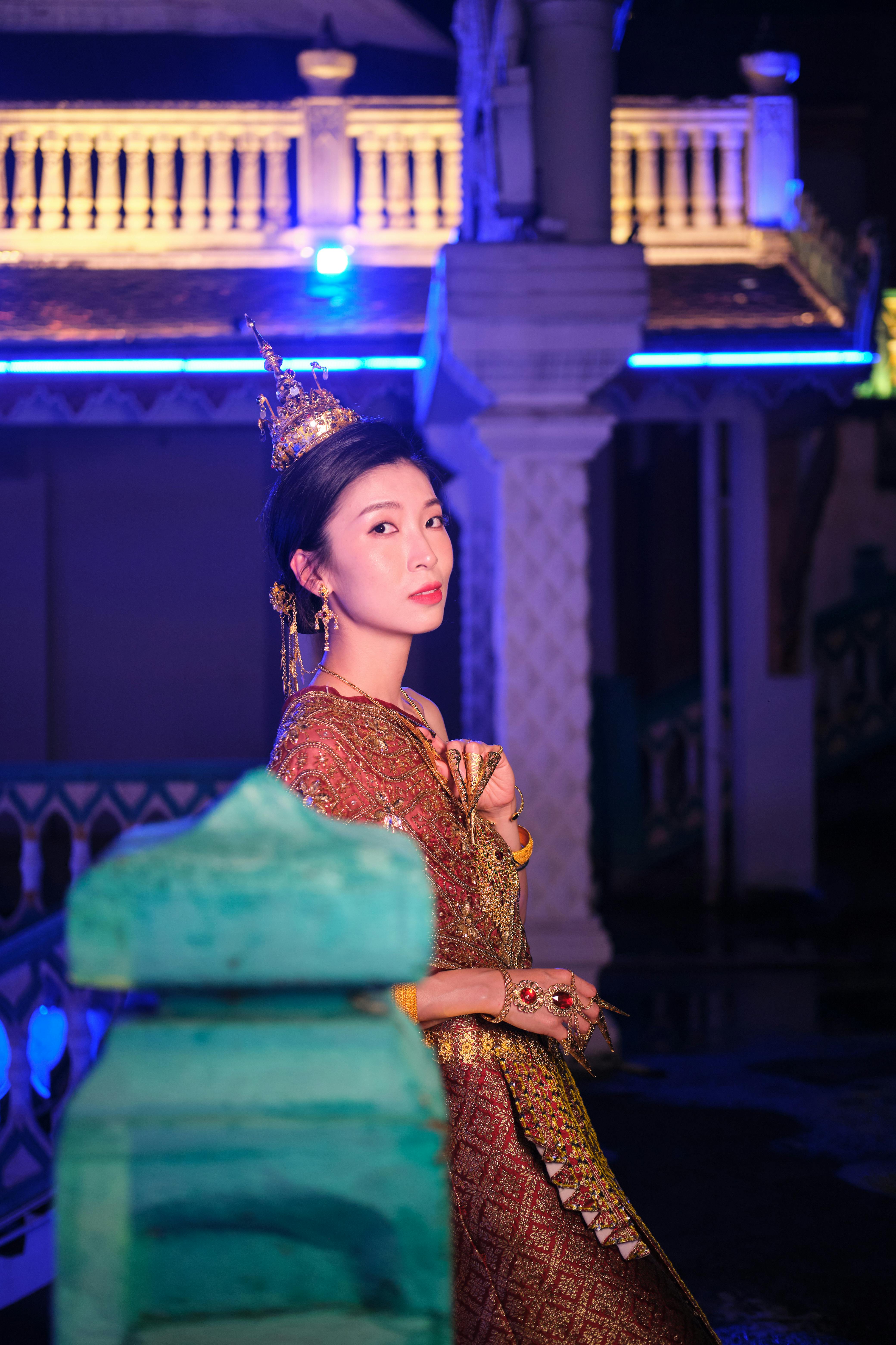 Portrait of an elegant woman in traditional attire posing at night with vibrant neon lights.