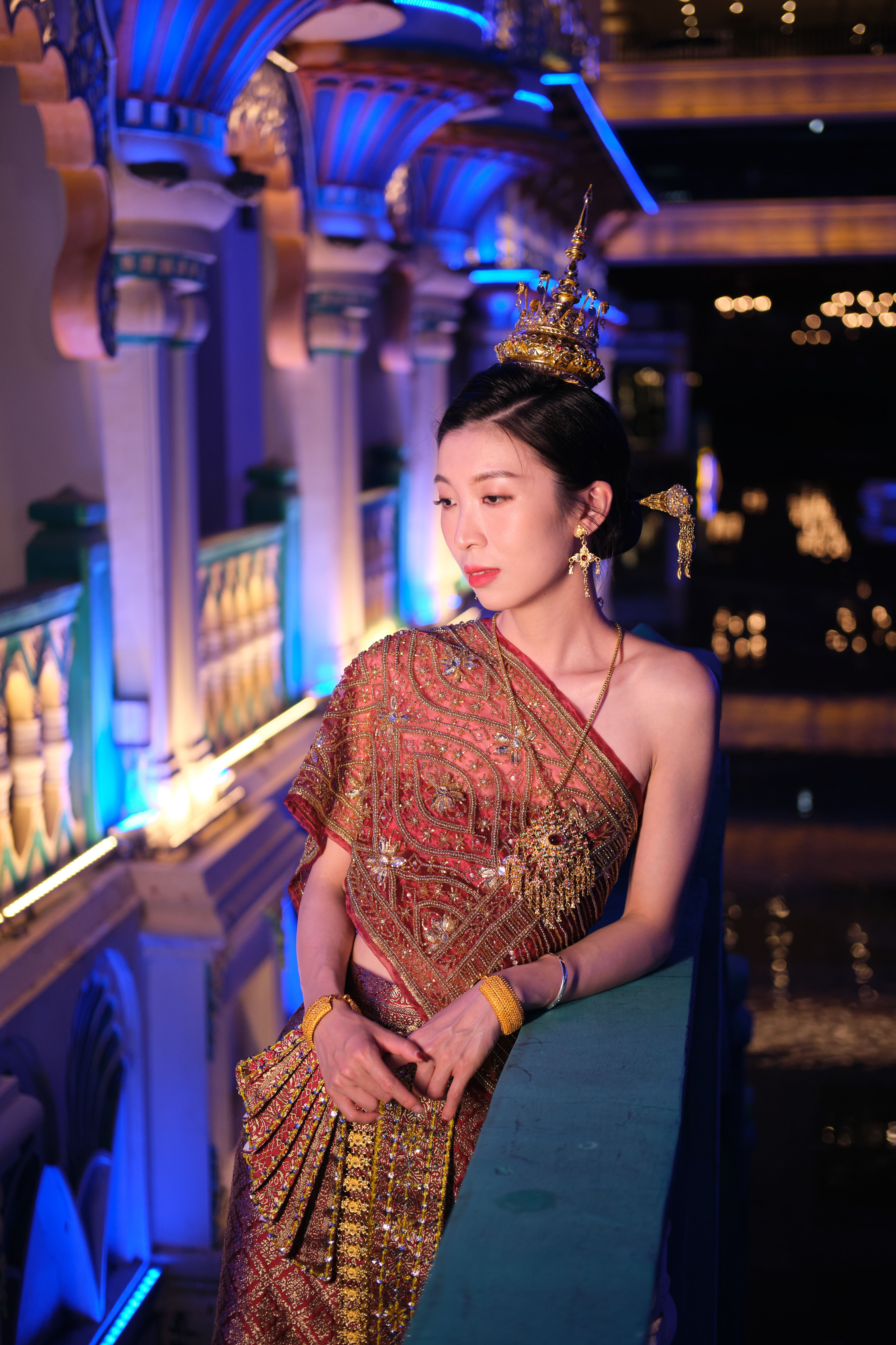 Portrait of an elegant woman in ornate traditional Thai dress, glowing under the night lights.