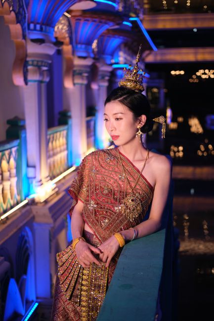 Portrait of an elegant woman in ornate traditional Thai dress, glowing under the night lights.
