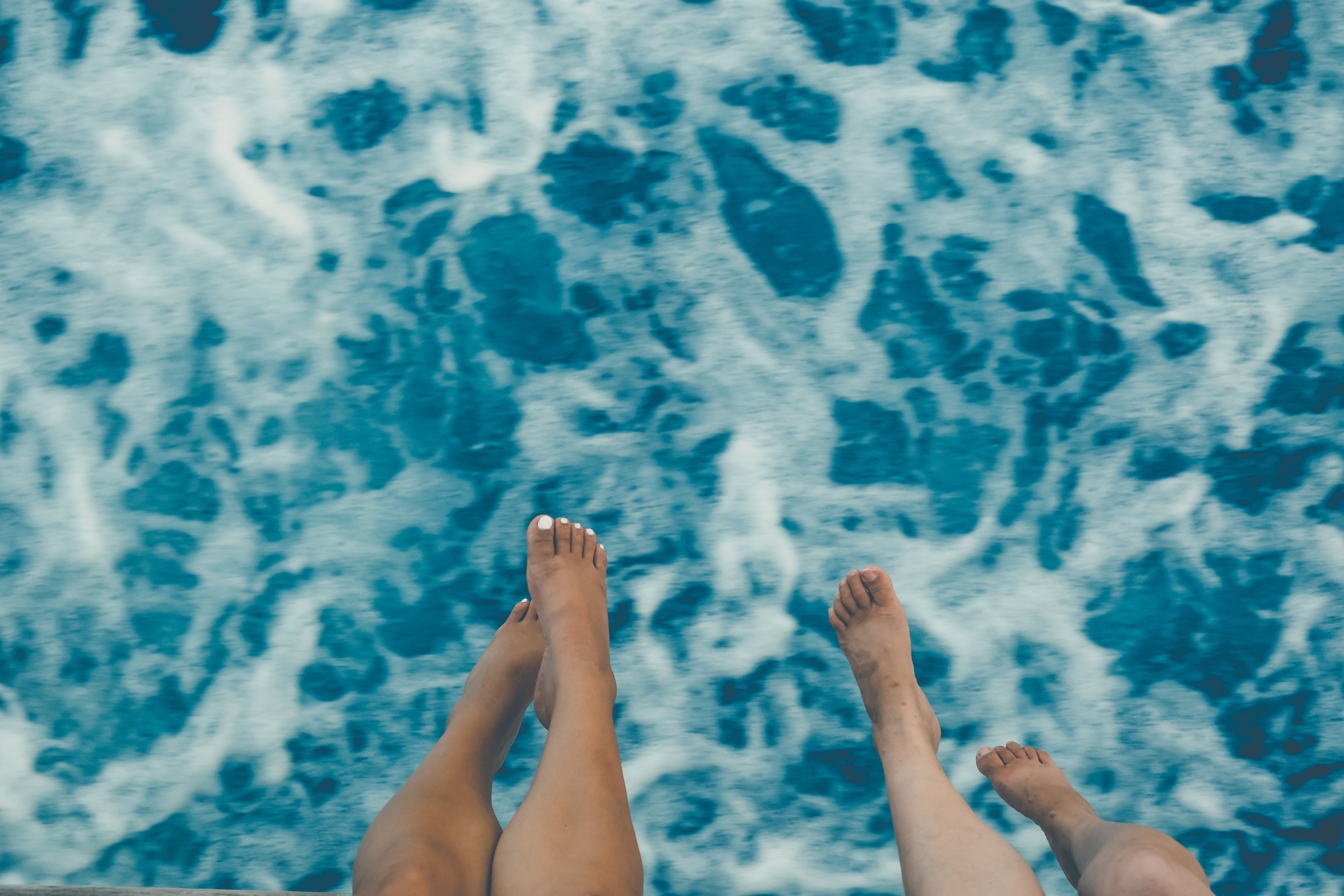 Two people with bare feet dangling above the ocean, capturing a summer vacation vibe.