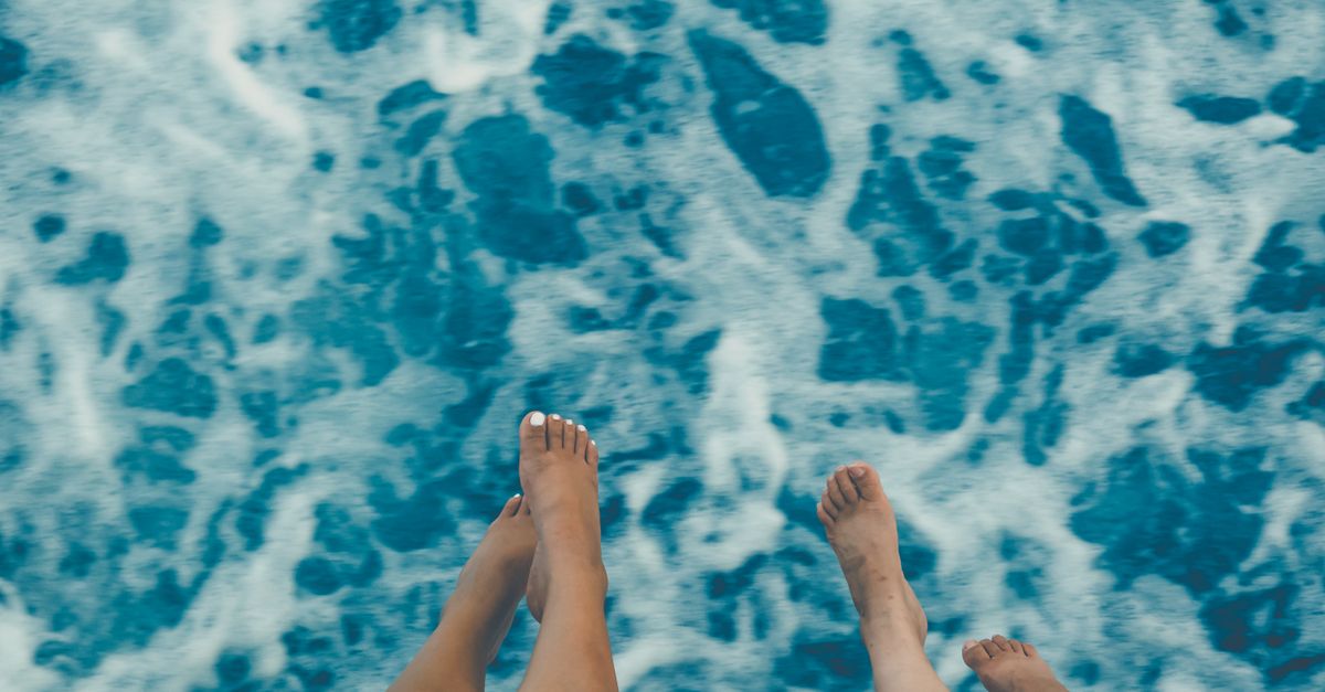 Two people with bare feet dangling above the ocean, capturing a summer vacation vibe.