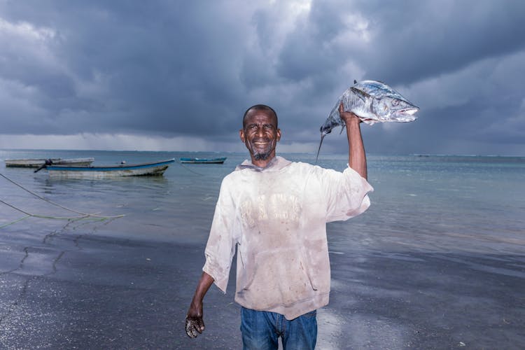 Man Holding Fish Near Body Of Water