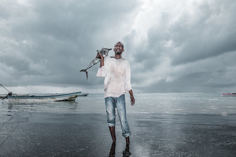 Man Holding Fish Near Body Of Water