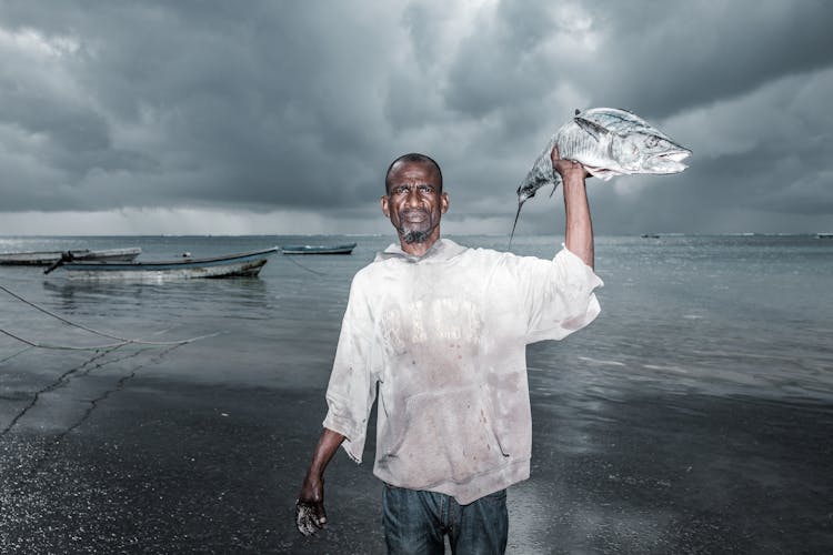 Man Holding Fish Near Body Of Water