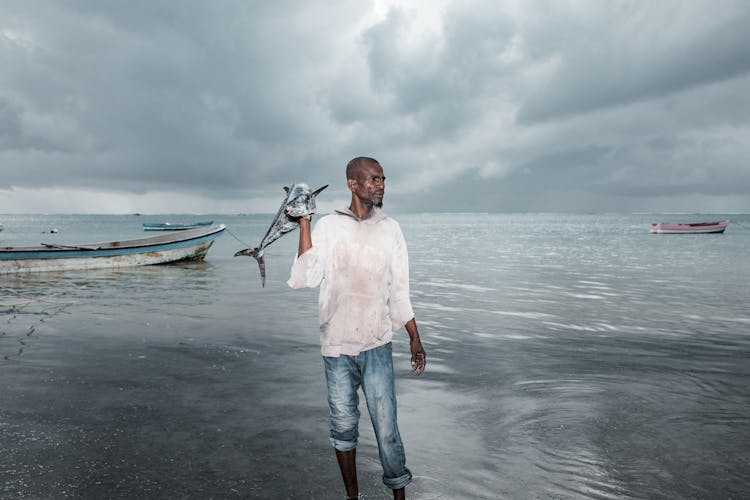 
Man Holding Fish Near Body Of Water