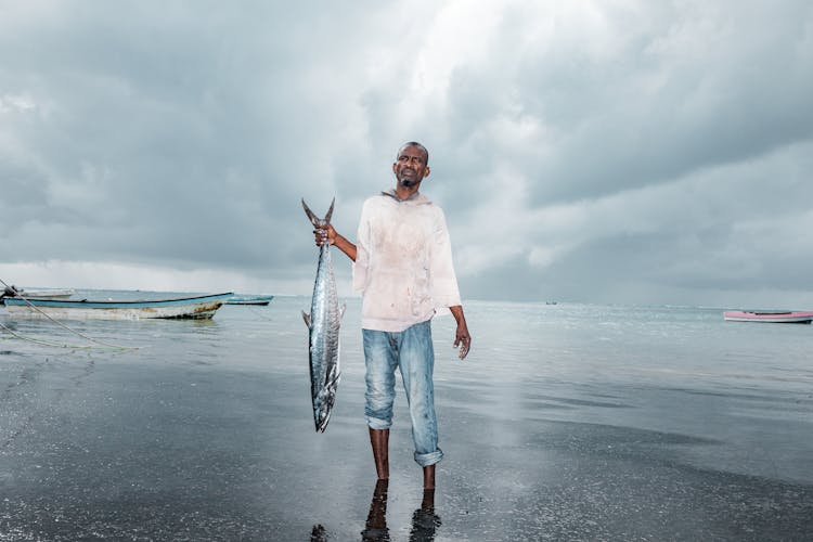 Man Holding Fish Near Body Of Water