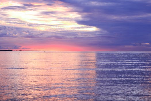 Tranquil sunset over the ocean, with a moody sky reflecting stunning colors on the water.