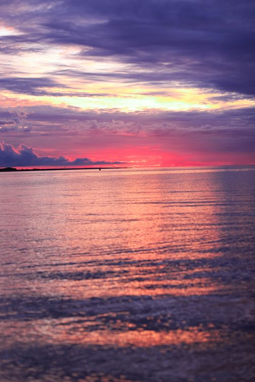 Free A serene sunset over a tranquil sea with vivid colors and moody sky. Stock Photo
