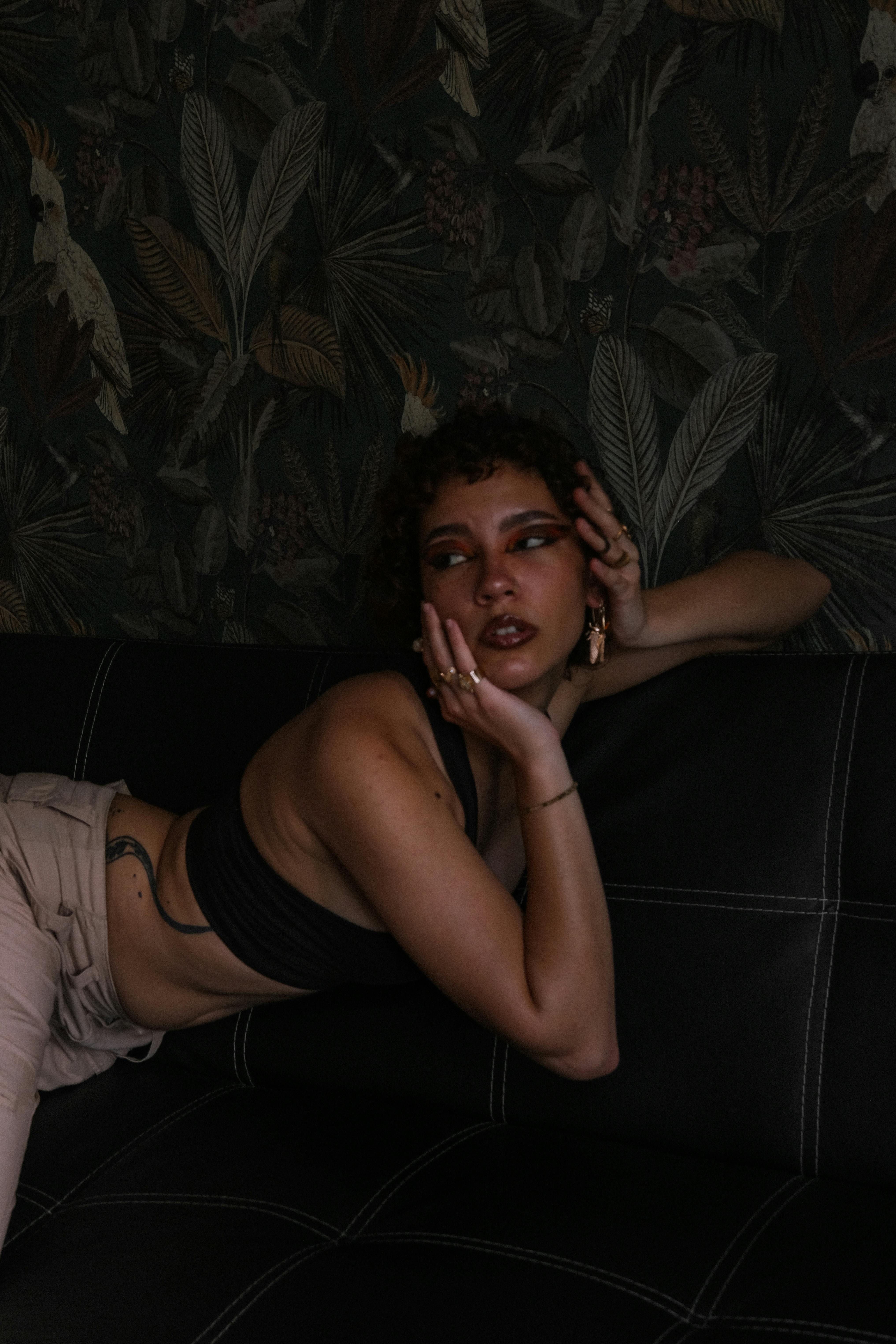 Fashionable woman in crop top posing on a black couch, creating a moody interior aesthetic.