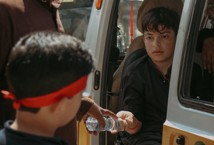 Boy Giving Bottle Water To A Man While Sitting Inside The Car
