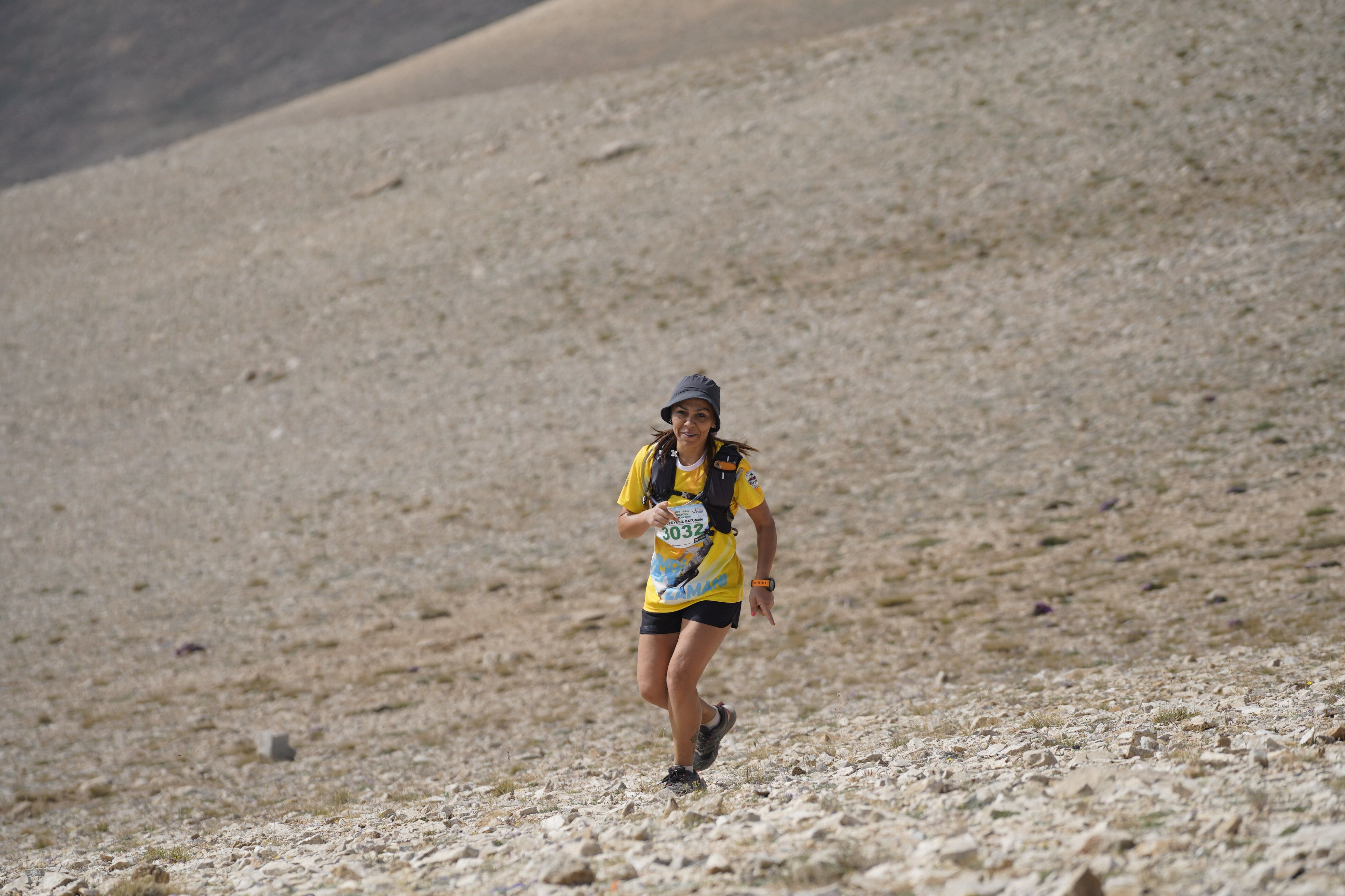 A smiling woman running uphill during a mountain adventure race.