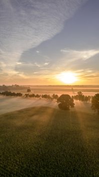 Beautiful aerial view of a sunrise over lush farmland with mist and trees.