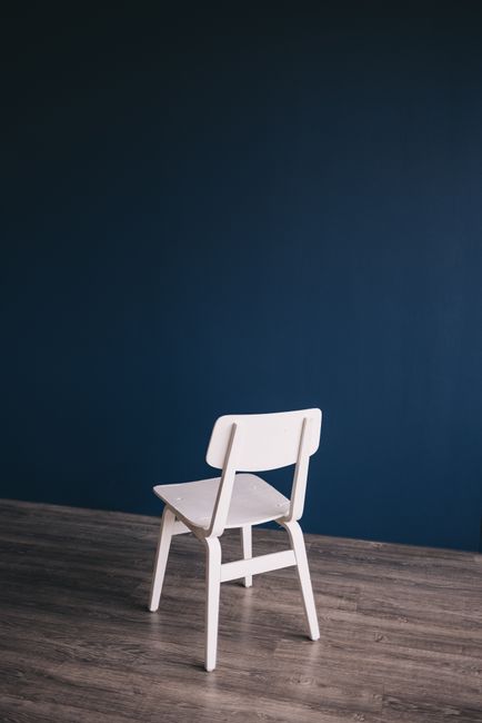 White chair on wooden floor with dark blue backdrop, perfect for modern interior design inspiration.