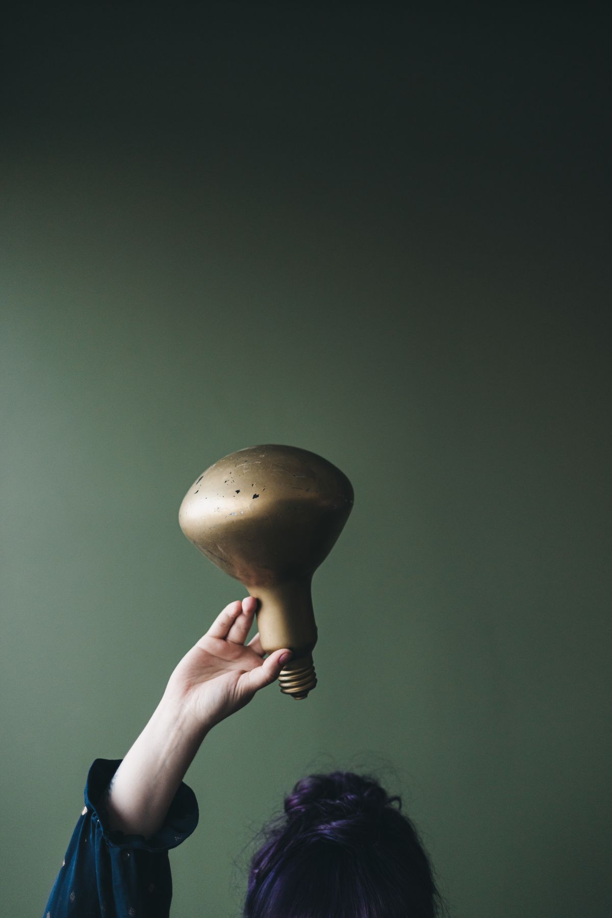 Person holding a metallic light bulb overhead, symbolizing a mindset shift