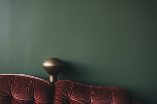 Free Elegant velvet sofa against a bold green wall with a vintage lamp adding character. Stock Photo