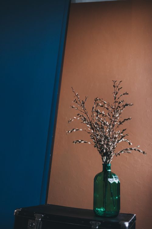 Free Artistic arrangement of dried plants in a vintage green bottle against a minimal blue and brown background. Stock Photo