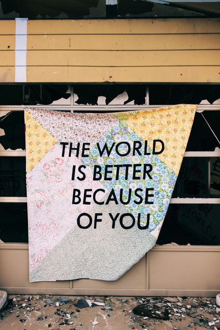 An inspiring message "The World is Better Because of You" displayed on a patchwork quilt hanging outside.