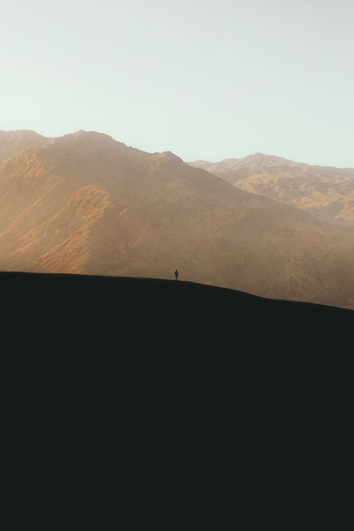 Free A solitary figure stands on a mountain against a sunrise backdrop, offering a serene and peaceful landscape. Stock Photo