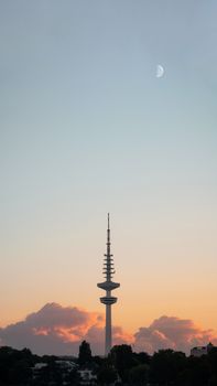 A serene view of the Heinrich Hertz Tower at twilight with a crescent moon overhead.