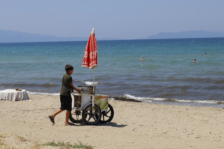 A Boy Pushing A Cart On A Beach