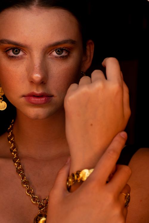 Free Close-up portrait of a woman elegantly displaying gold jewelry, featuring earrings and a bracelet. Stock Photo