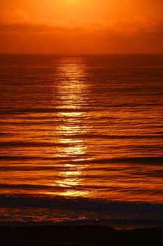 Capture of a vibrant sunset over the ocean, casting a golden glow on the water's surface.