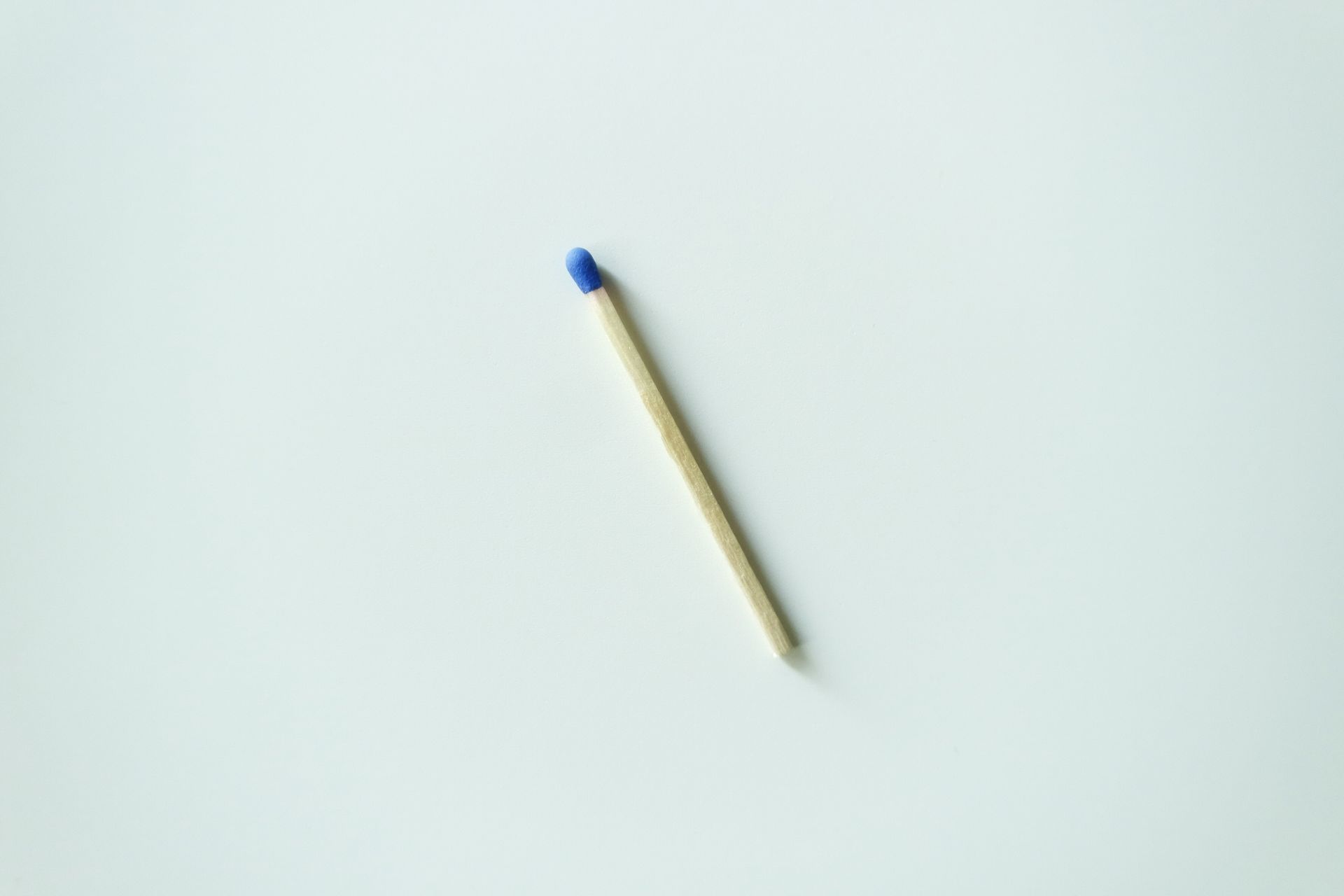Single matchstick with a blue tip on a clean white surface, minimalistic style.