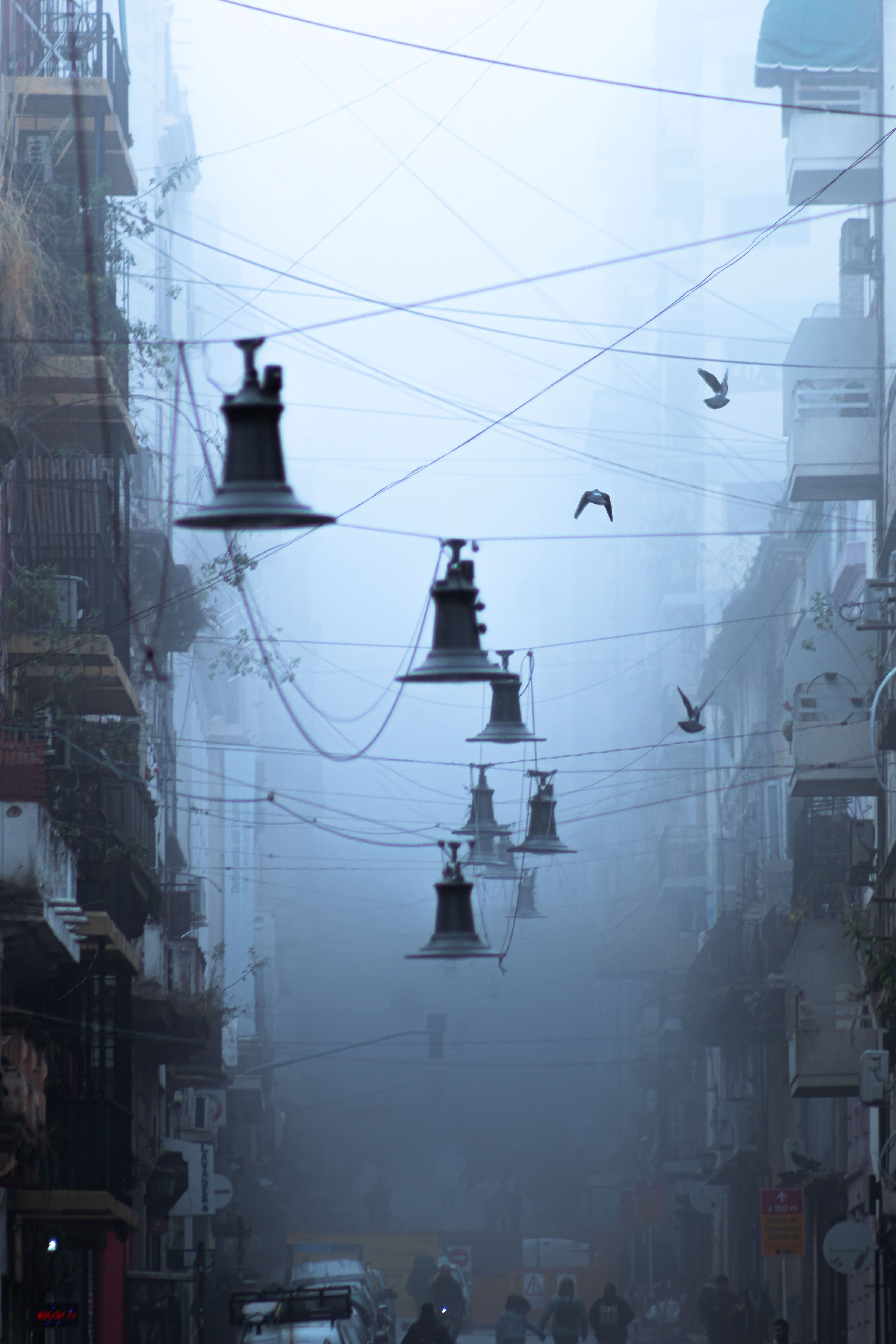 Misty urban street scene with hanging bell-shaped lamps and visible power lines.