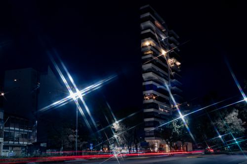 Free A tall modern building illuminated by streetlights and light trails on a city street at night. Stock Photo