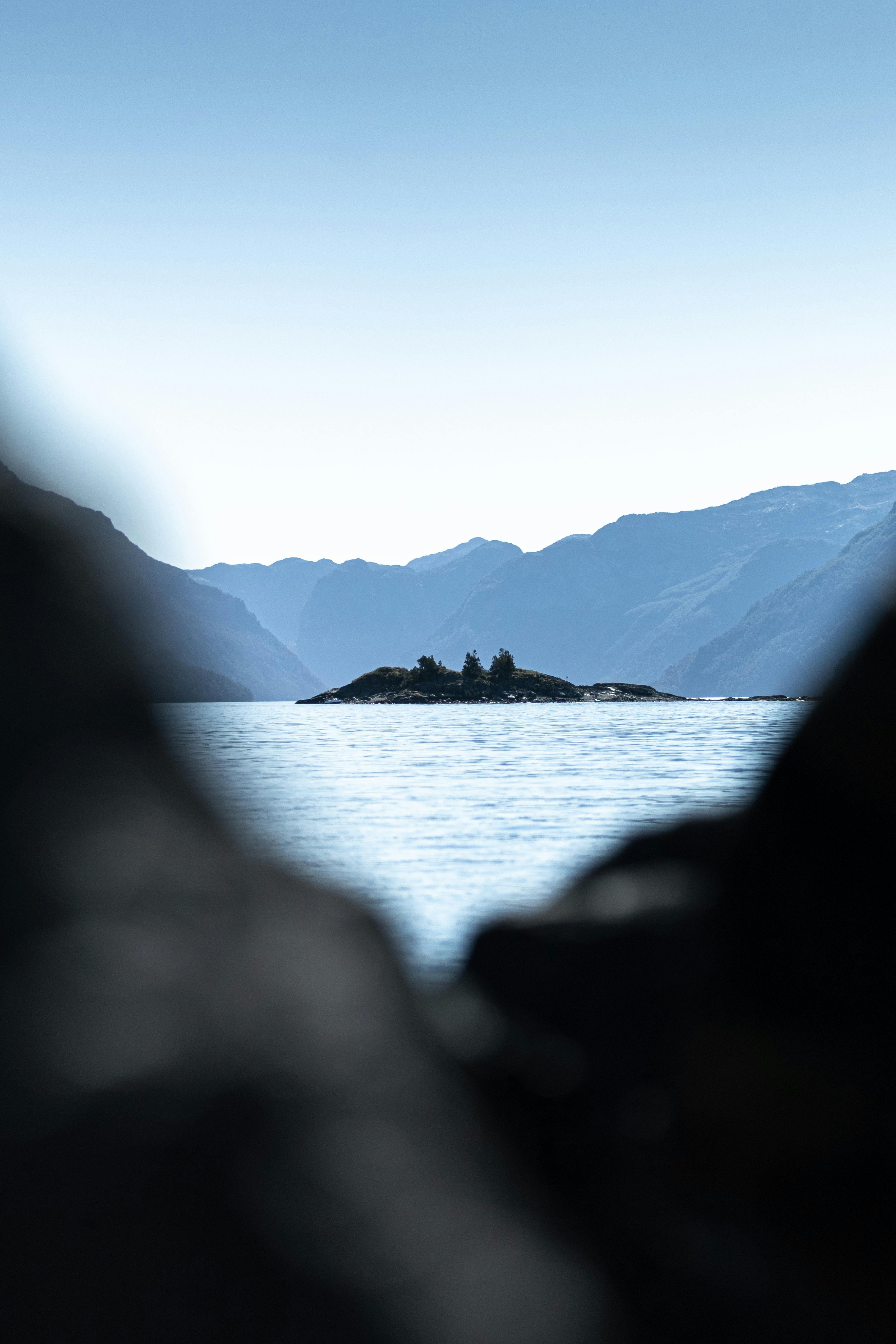Tranquil view of a small island surrounded by water with majestic mountains in the background.