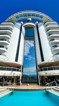 Tall cruise ship featuring sleek modern design with reflective glass and pool, captured in Genoa, Italy.