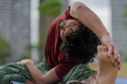 Adult male doing a yoga stretch in an outdoor setting, focusing on flexibility and relaxation.