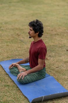 A man meditating in a relaxed posture on a blue yoga mat in a grassy field.