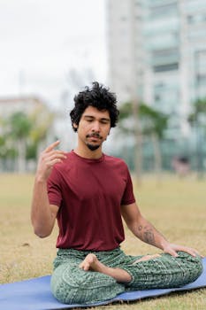 A man sits cross-legged on a yoga mat meditating in a city park.