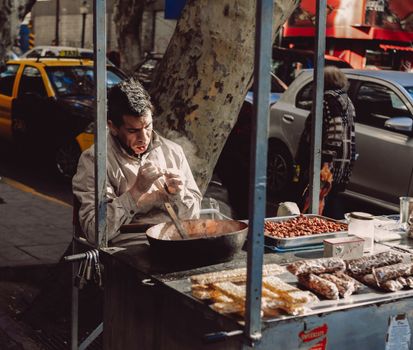A street vendor prepares food on a busy city street, surrounded by cars and pedestrians.