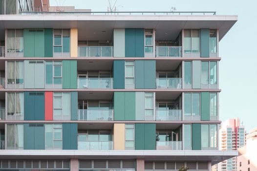 Vibrant modern apartment building facade with glass balconies under a clear blue sky.