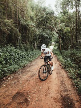 Man in cycling gear biking down a dirt road through a lush forest.