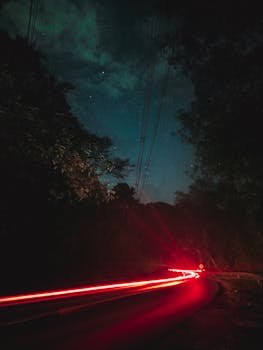 Long exposure photo capturing trailing red lights from cars on a winding road at night.
