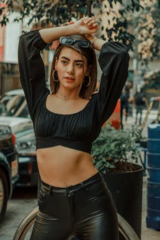 Confident woman in black crop top and leather pants posing outdoors.