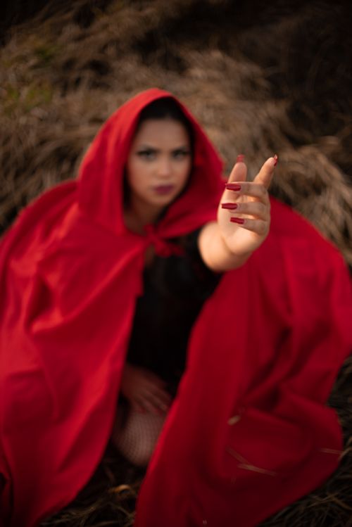 Free Woman in a red cloak extends her hand dramatically in an outdoor setting with blurred background. Stock Photo