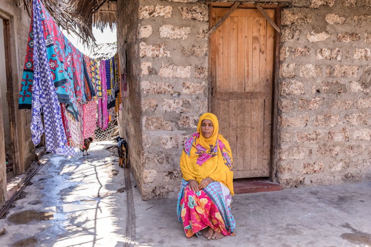 Old Woman In Headscarf Sitting On Street In Poor Village