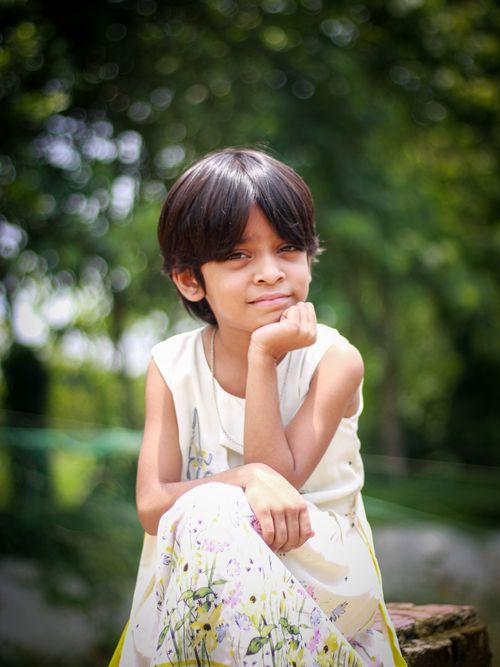 Free A young girl sitting outdoors with a thoughtful expression against a natural, blurred background. Stock Photo