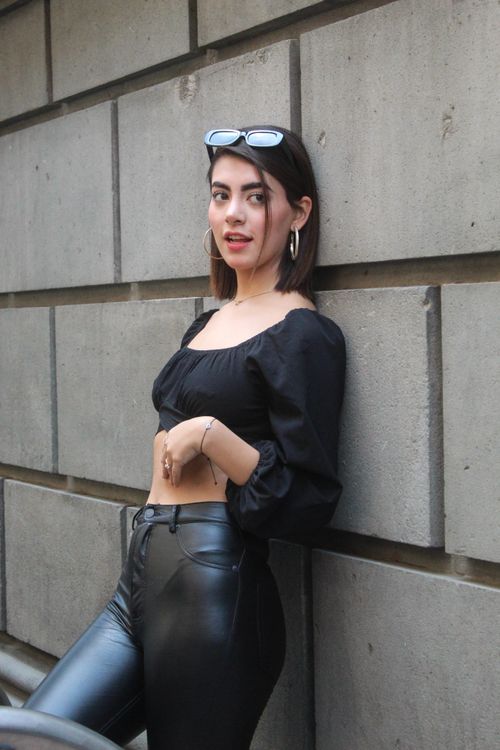 Free Fashionable woman in black leather pants leaning against an urban wall, showcasing style and confidence. Stock Photo