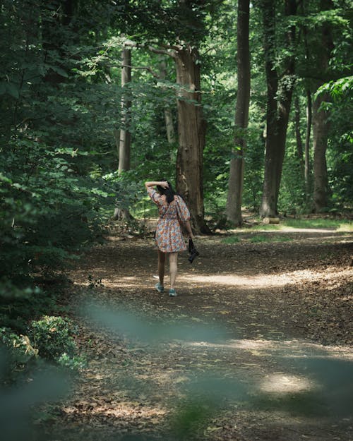 A Woman Walking Beside Green Trees