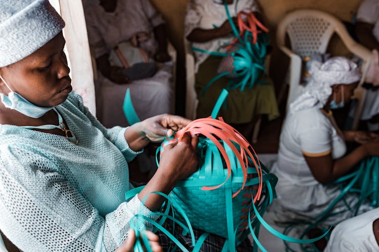 Women Sitting Together  In A Room While Weaving A Plastic Basket