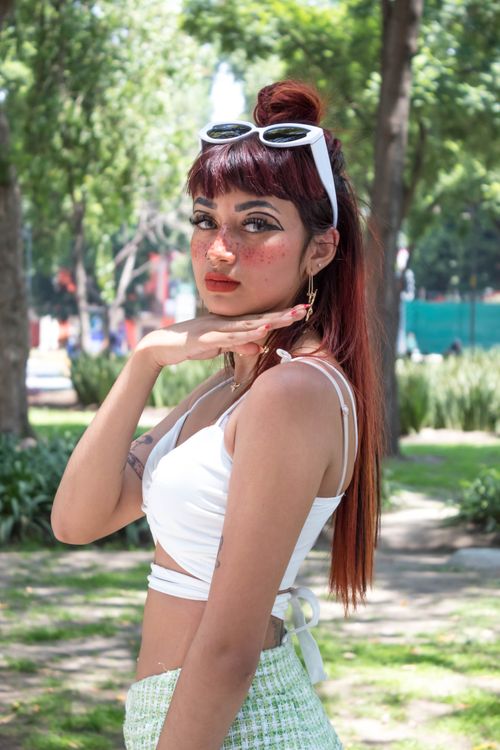 Free Fashionable woman posing with hand under chin in a sunny park in Mexico City, showcasing summer style. Stock Photo