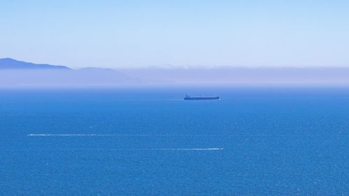 Free A serene view of a container ship on the ocean horizon under clear skies. Stock Photo